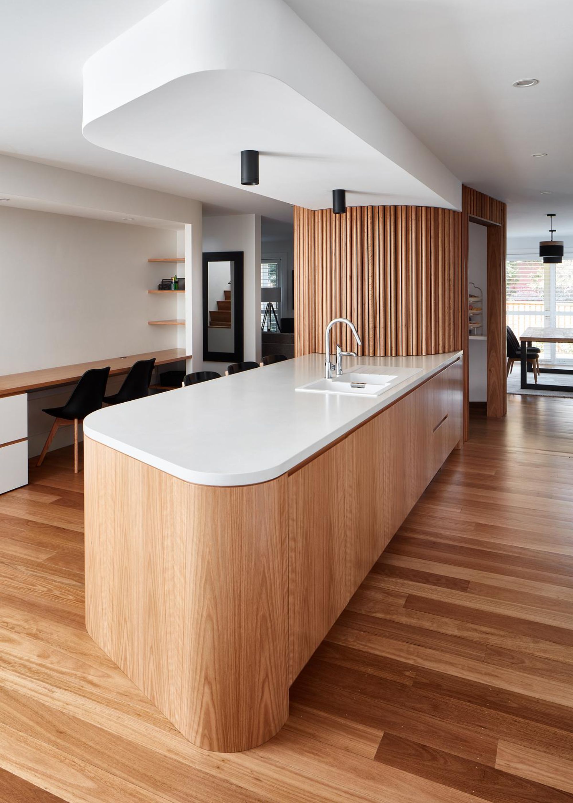 A large open-plan kitchen with an island in the middle that has quartz worktops on top as well as a sink within the worktop. There is also a view of the rest of the home