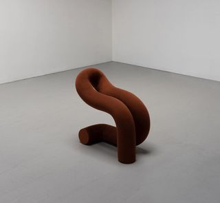 A chair made by twisting a tube upholstered in brown textile
