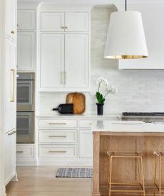 A white kitchen with a wooden kitchen island, gold hardware, and a hard wood floor