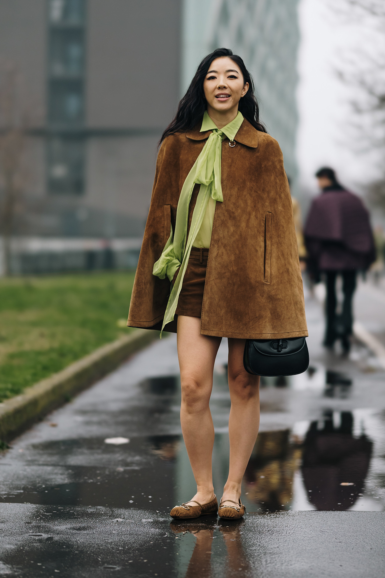 a fashion week attendee wears a suede cape, green tie blouse, mini skirt, and mary jane flats