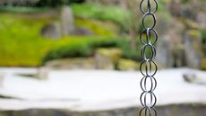 A rain chain in focus in front of a blurry garden