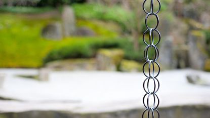 A rain chain in focus in front of a blurry garden