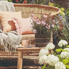 A garden with a rattan garden bench and a flower pot on a side table in front of it