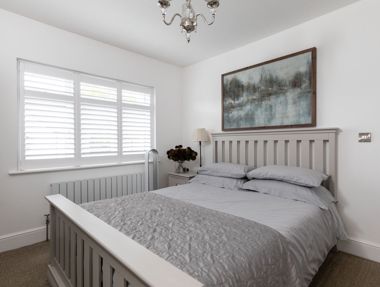 A bedroom with a double bed with grey sheets and a large window with shutters