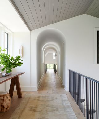landing with wooden console, wooden floor, patterned rug, white shiplap ceiling and archway