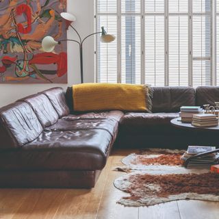 A brown leather modular corner sofa in a living room with a colourful artwork hanging behind it