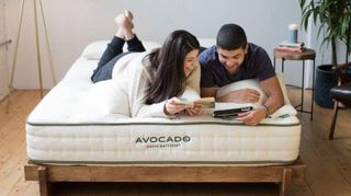 Avocado mattress sale, promo codes and deals: a couple lie on the Avocado Green mattress while looking at photos