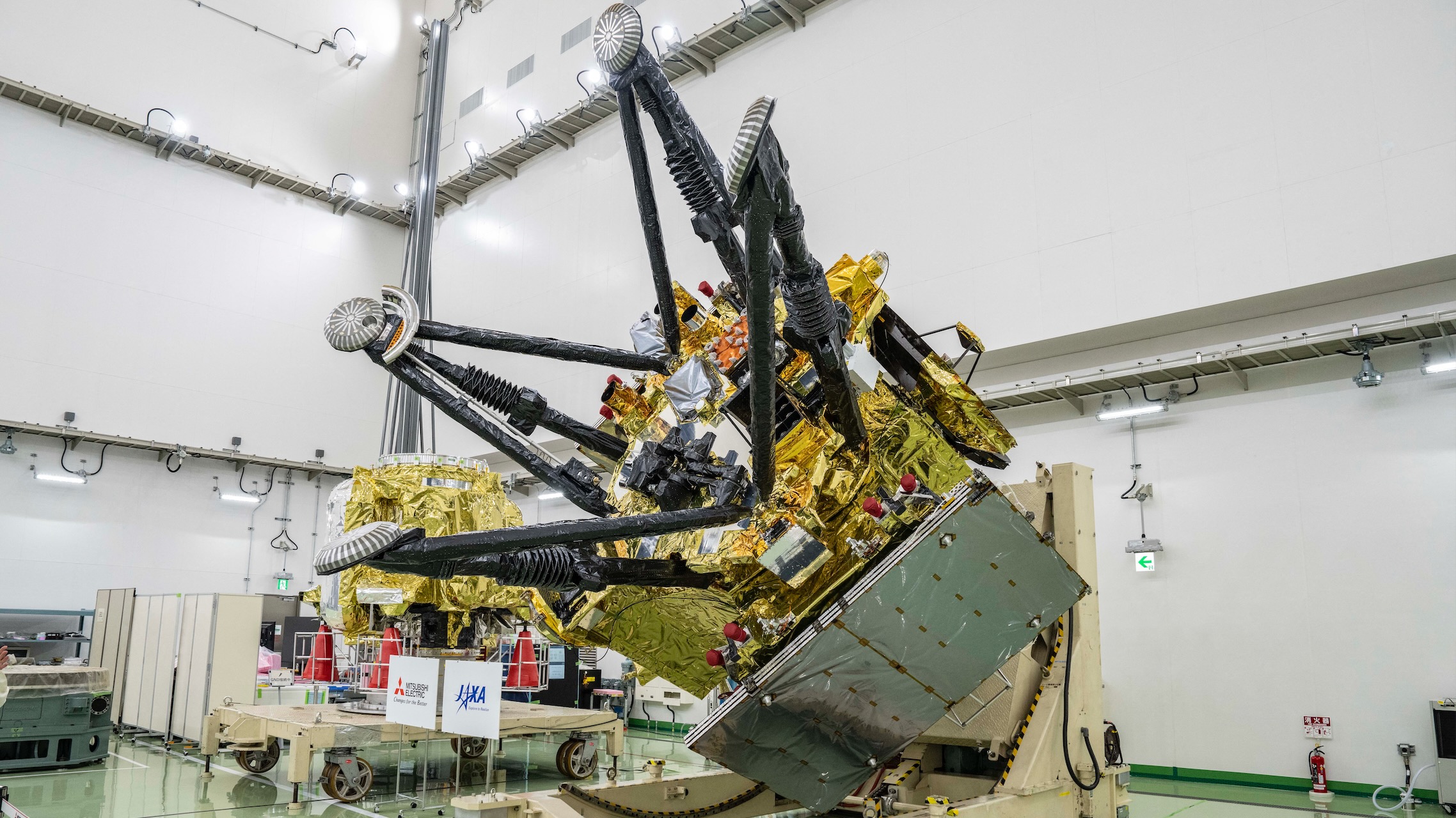 two large, gold-foil-wrapped spacecraft sit inside a large white-walled cleanroom
