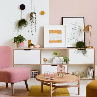 Living room with white and pink walls, pink armchair and whit and wood storage unit