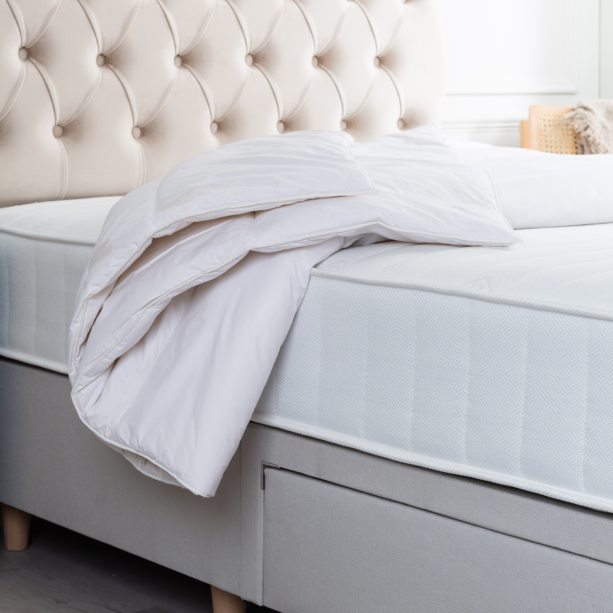 The Slumberdown Wonderful Wool Duvet draped over a mattress on a bed with an upholstered cream headboard