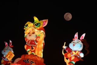 a full moon can be seen in the night sky behind three colorful lanterns shaped like smiling animals