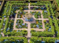 A gardener pictured amongst the stunning flower garden, full of forget-me-nots, wallflowers, euphorbia, tulips and other spring flowers at Loseley Park Gardens in Guildford, Surrey, photographed by drone. RHS Photographic Competition 2021. ©Oliver Dixon