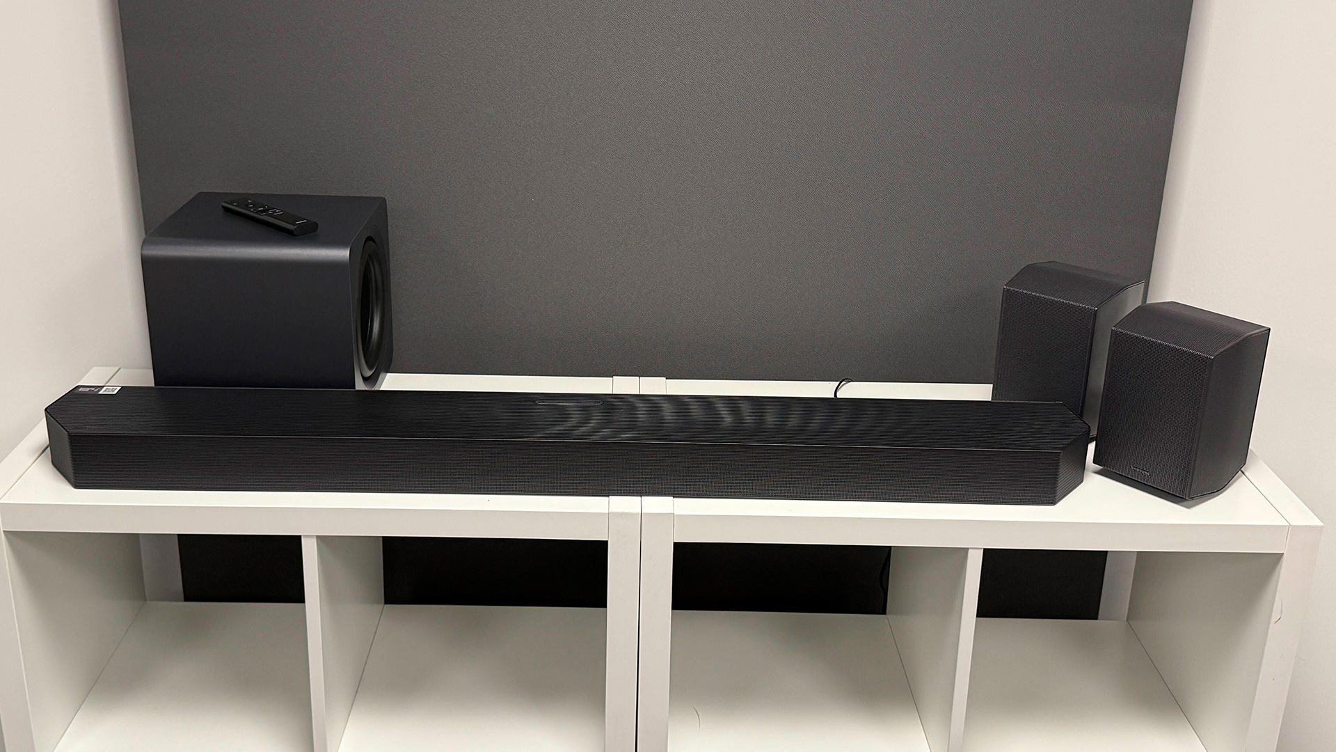 Samsung HW-Q990H soundbar package on white wooden shelf unit in front of grey baffle
