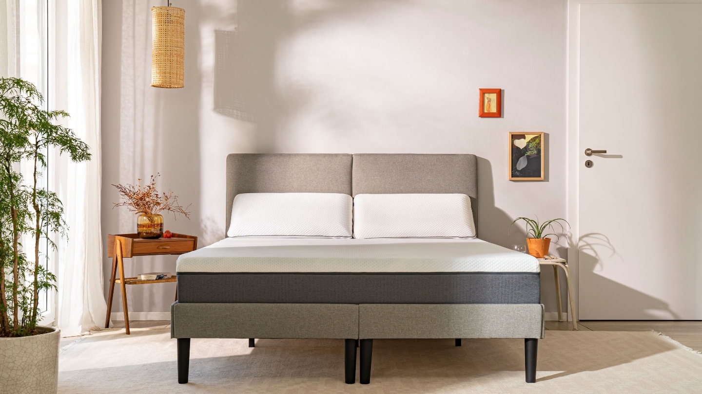 A bedroom with a bed in the middle with a mattress and bed side tables on either sides and plants around it