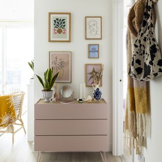 Pink chest of drawers in a small hallway with a gallery wall on top of it.