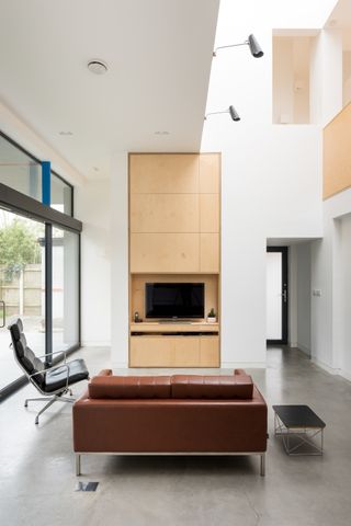 bauhaus inspired living room with concrete floor, timber cabinetry, leather sofa and armchair and tall ceilings