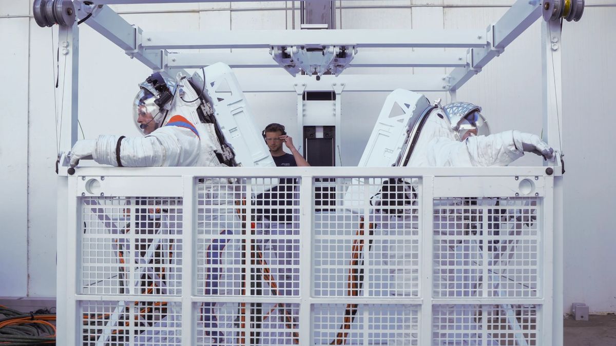 astronauts in white spacesuits stand inside a white airlock