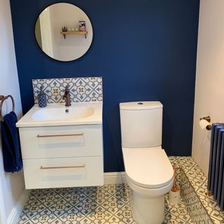 bathroom with blue wall and round mirror and blue towel and toilet and washbasin