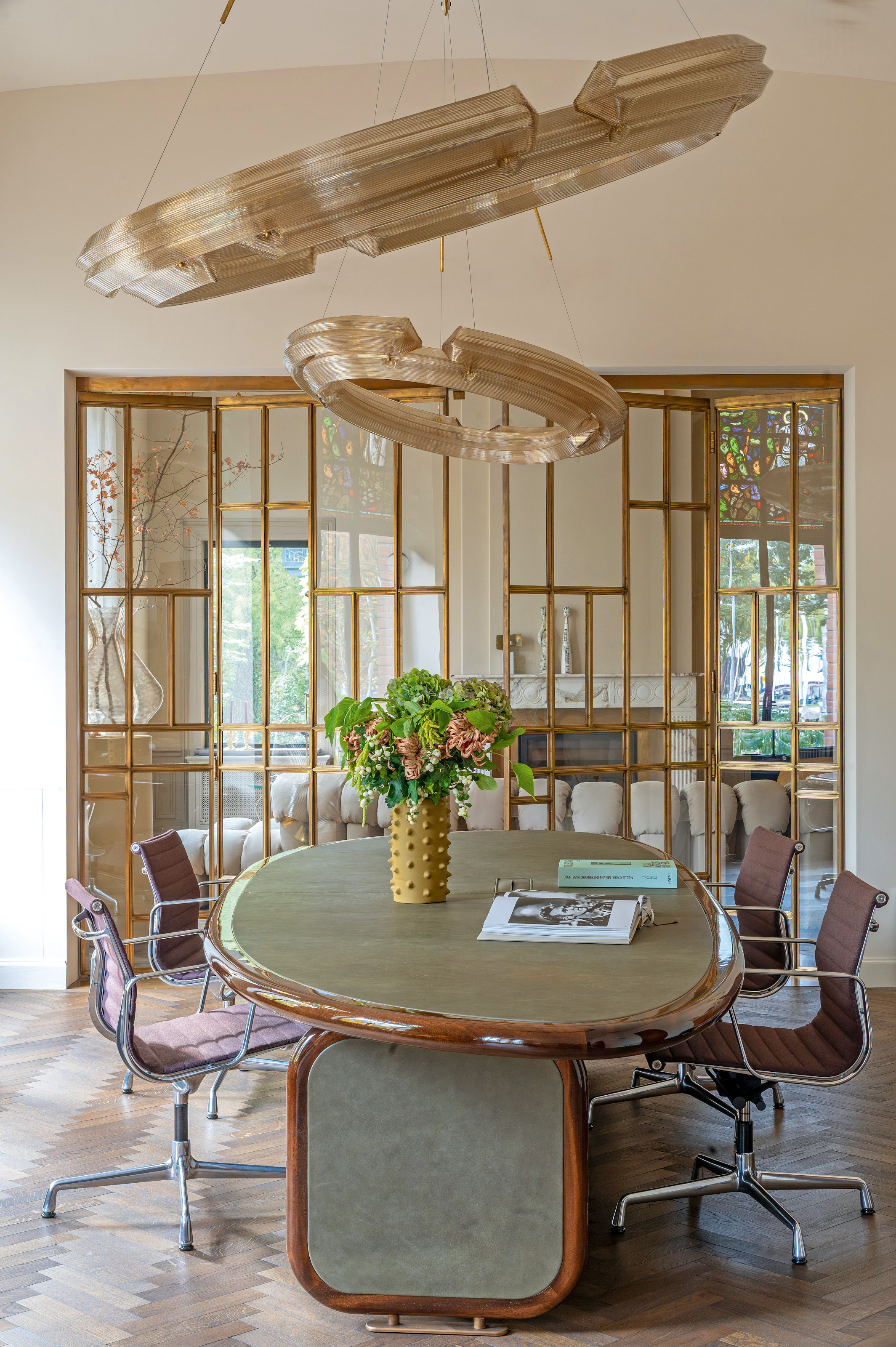 Office with gold glass screens, green and wood oval table, chrome desk chairs and yellow vase
