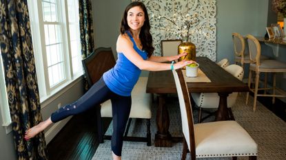 Woman exercising in a dining room, holding the back of a chair