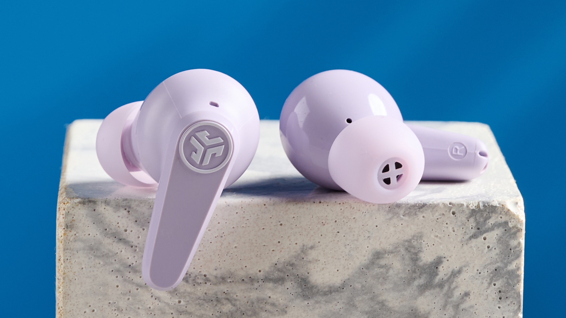 the jlab go pods anc earbuds in lilac with a lilac charging case and built in usb-c cable against a blue background on a marble stand