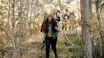 A group of smiling people in outdoor apparel hike in a forest setting