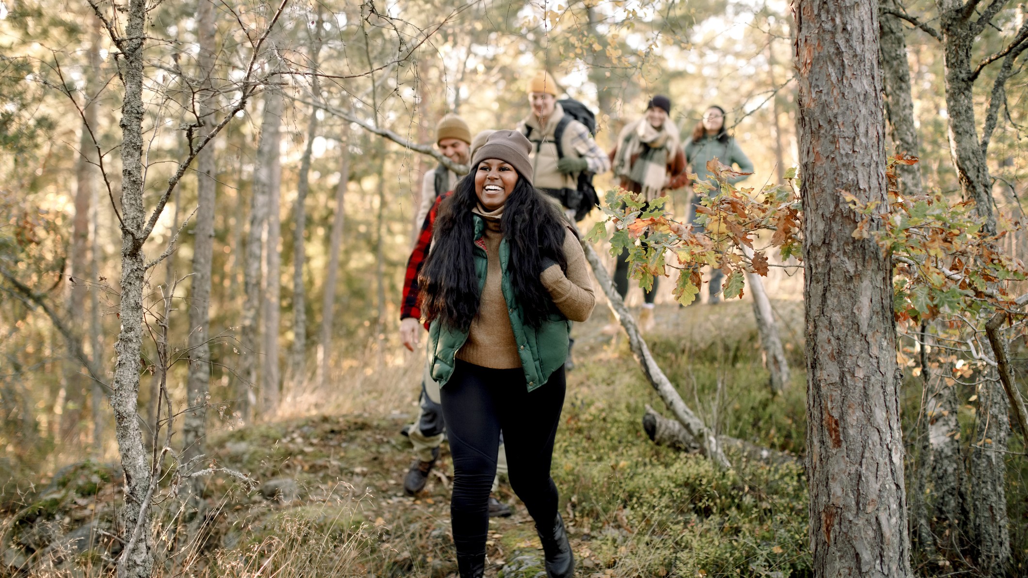 A group of smiling people in outdoor apparel hike in a forest setting