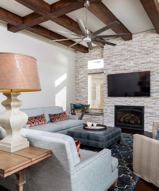 living room with white wall, wooden beamed ceiling, brick wall with tv and neutral sofas