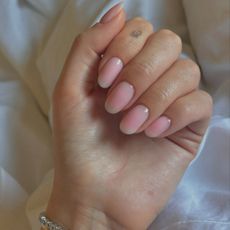 A woman's hand on a white bed sheet with a blurred French tip nail design