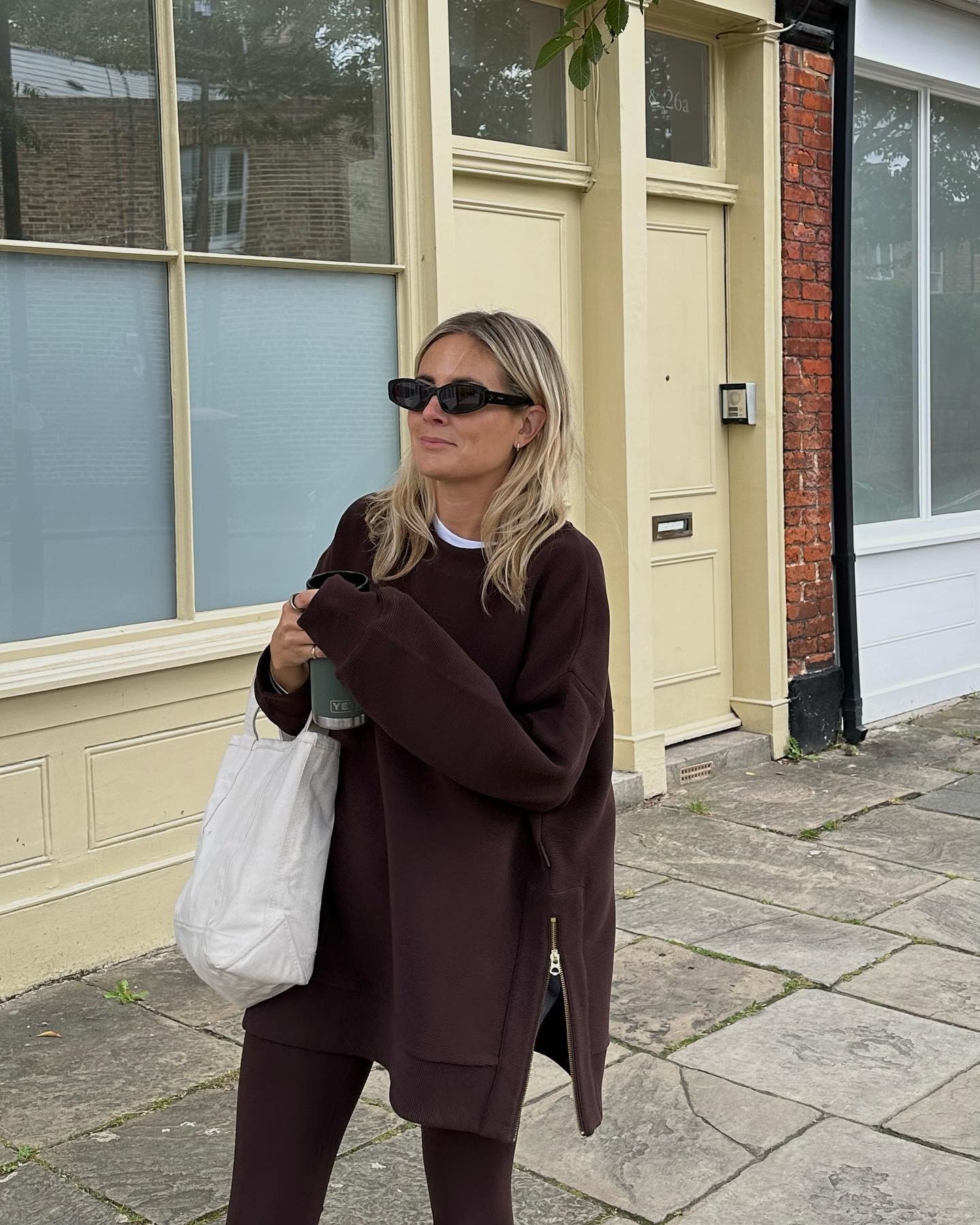 Influencer @lucywilliams02 stands outside in London wearing burgundy leggings with a burgundy jumper and black sunglasses.