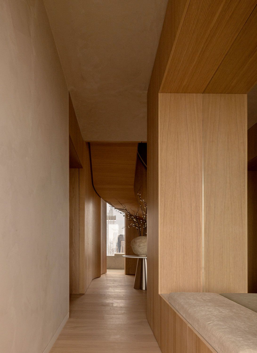 Oak-lined corridor at 262 Fifth Avenue by Norm Architects, with integrated seating, sculptural joinery, and a framed glimpse of the Manhattan skyline beyond
