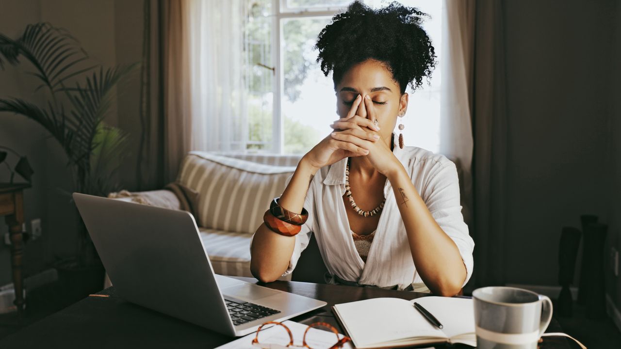 A woman appears to be frustrated whilst sitting at her desk with her hands over her face