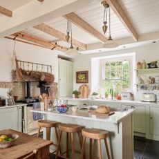 modern country farmhouse kitchen with pale green units, island with stools and cream range cooker in old stone inglenook