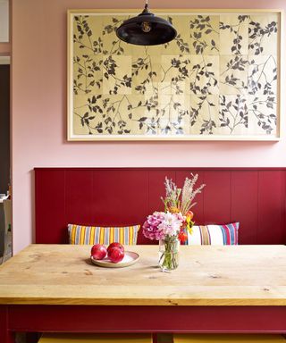 pink kitchen diner with red bench and red table with wooden top, yellow stools, statement artwork and gray pendant