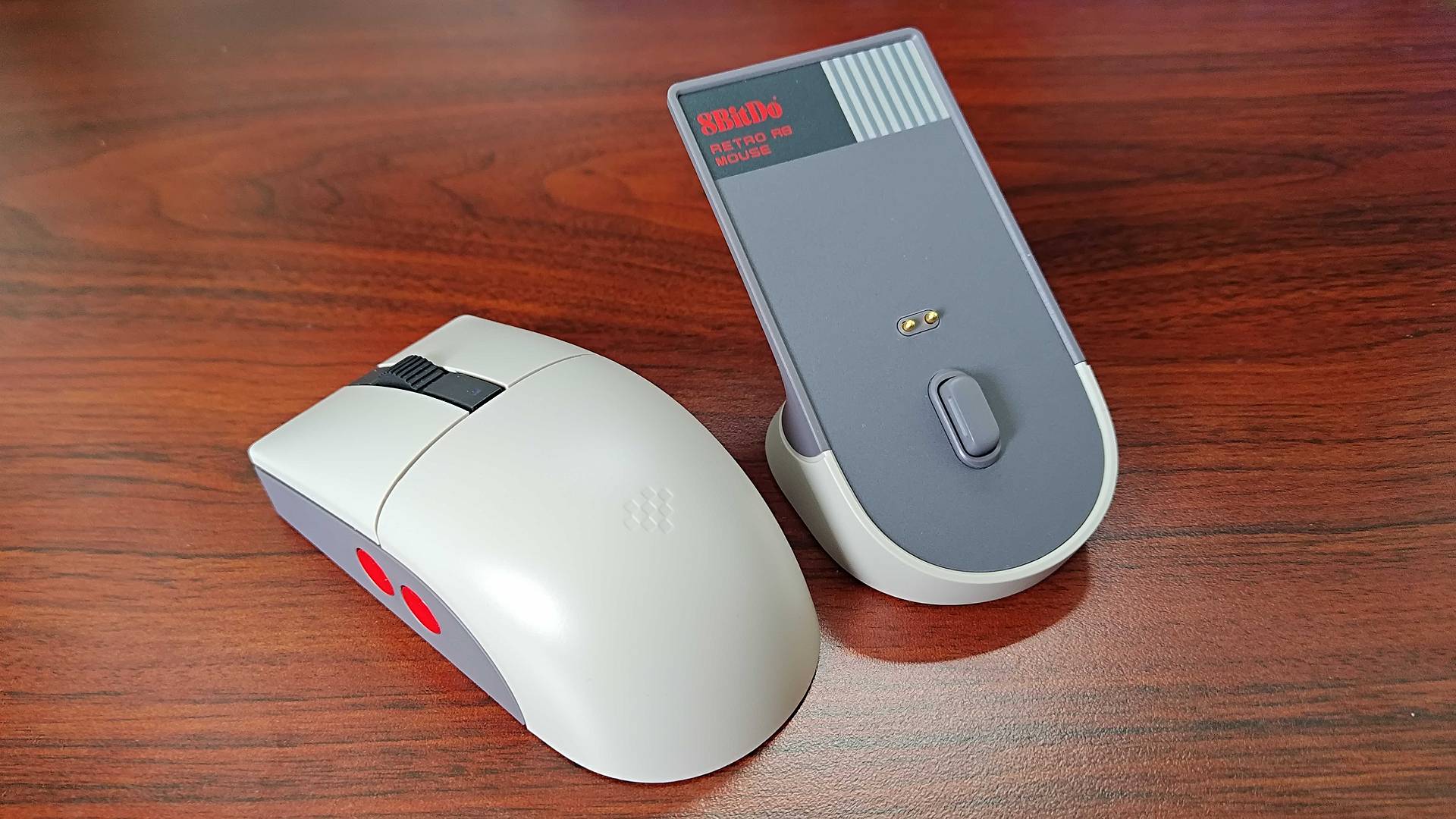 8Bitdo Retro R8 mouse on woodgrain desk removed from charger stand.