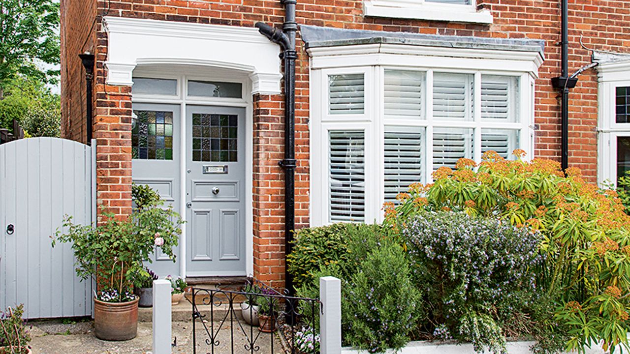 Front of red brick house with hedge and bay window