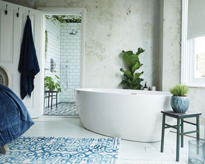 Contemporary, light and bright bedroom with bath in the corner of the room, textured white walls, white painted wooden flooring, blue decorative vases, rug and bedding, looking on into ensuite