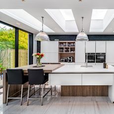 White modern kitchen with skylights, pendant lighting and two level island