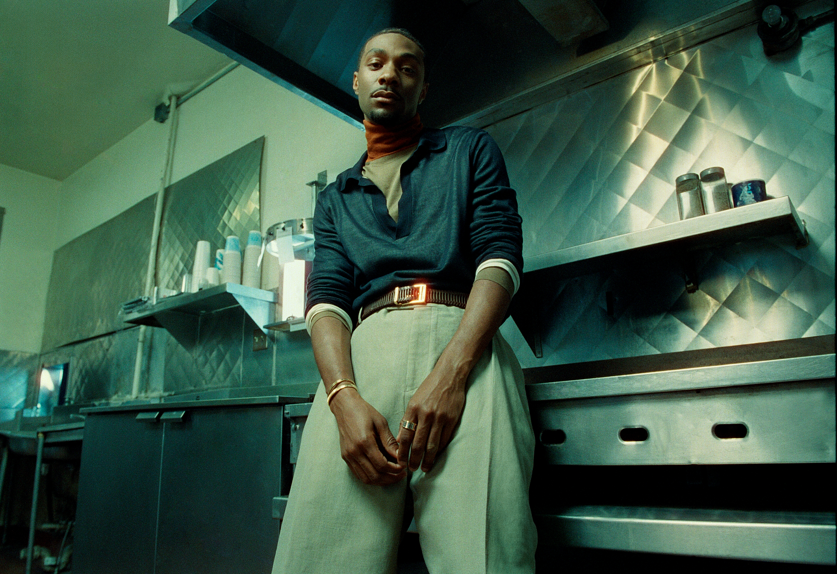 Jonathan Daviss wears a layered long-sleeve and trousers with a belt.