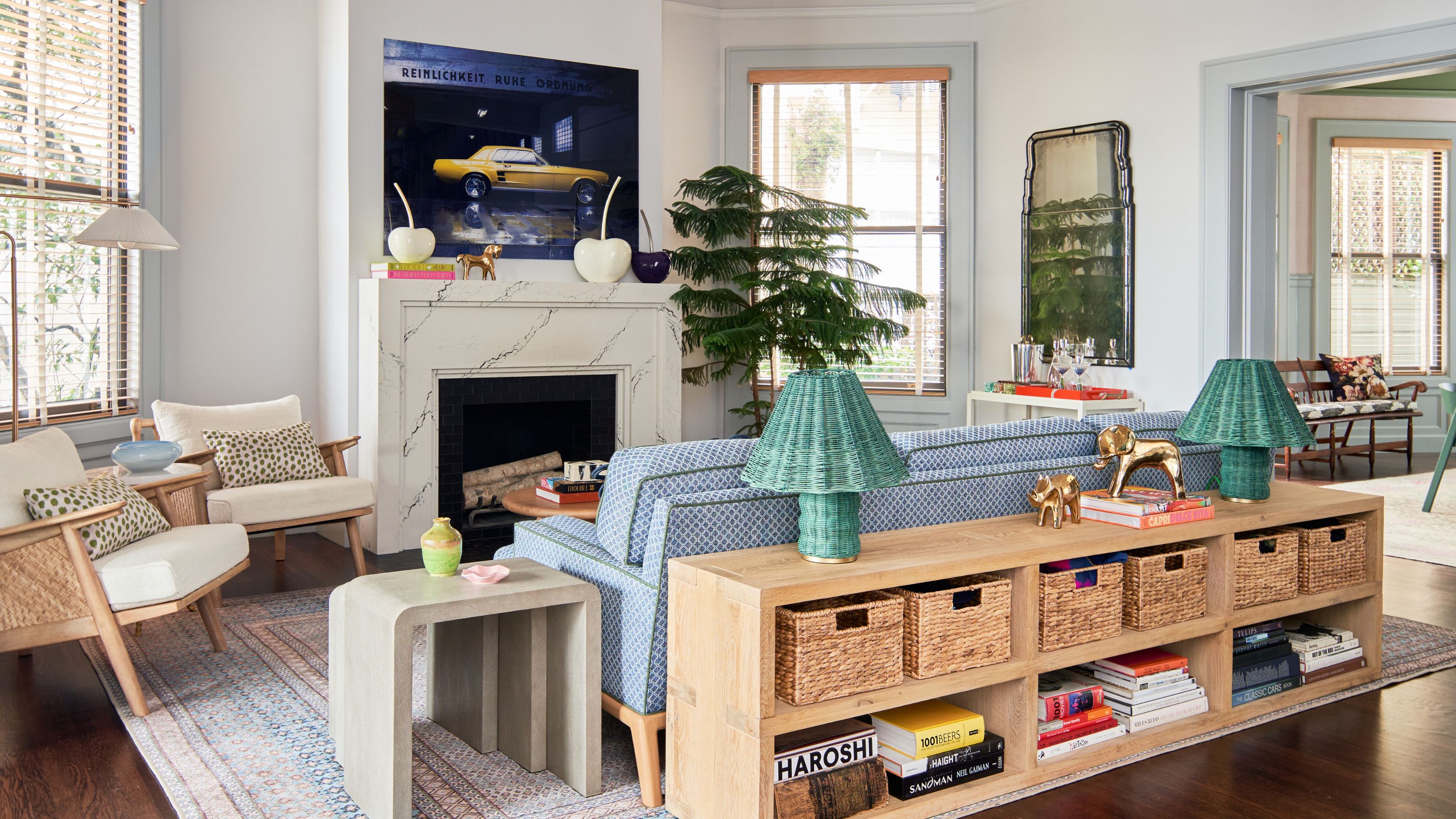 neutral living room in a San Francisco home designed by Studio Monroe with a marble fireplace, blue couch, sofa table with green lamps and two rattan neutral armchairs