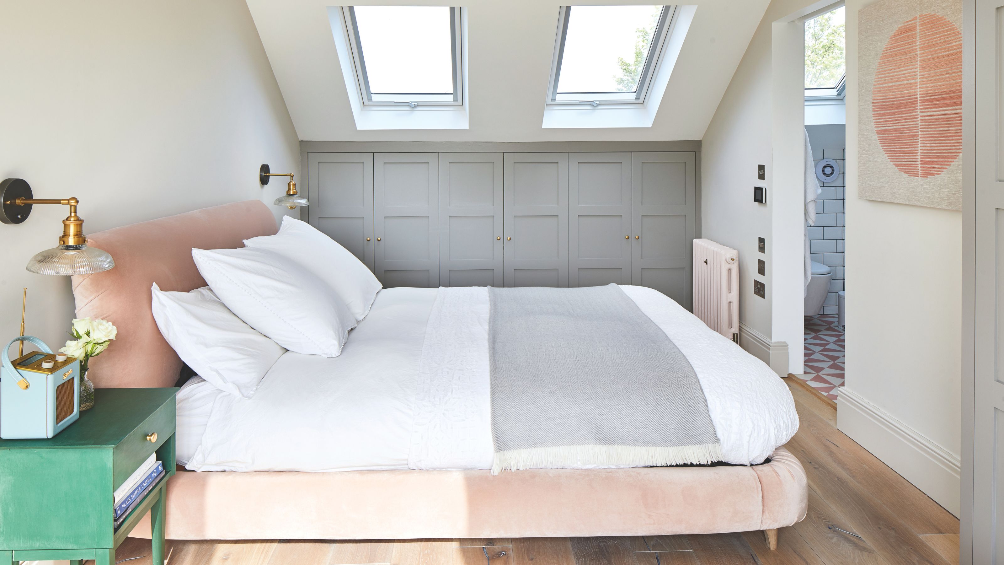 White painted loft bedroom with built-in blue wardrobes and a pink bedframe with white bedding in the middle 