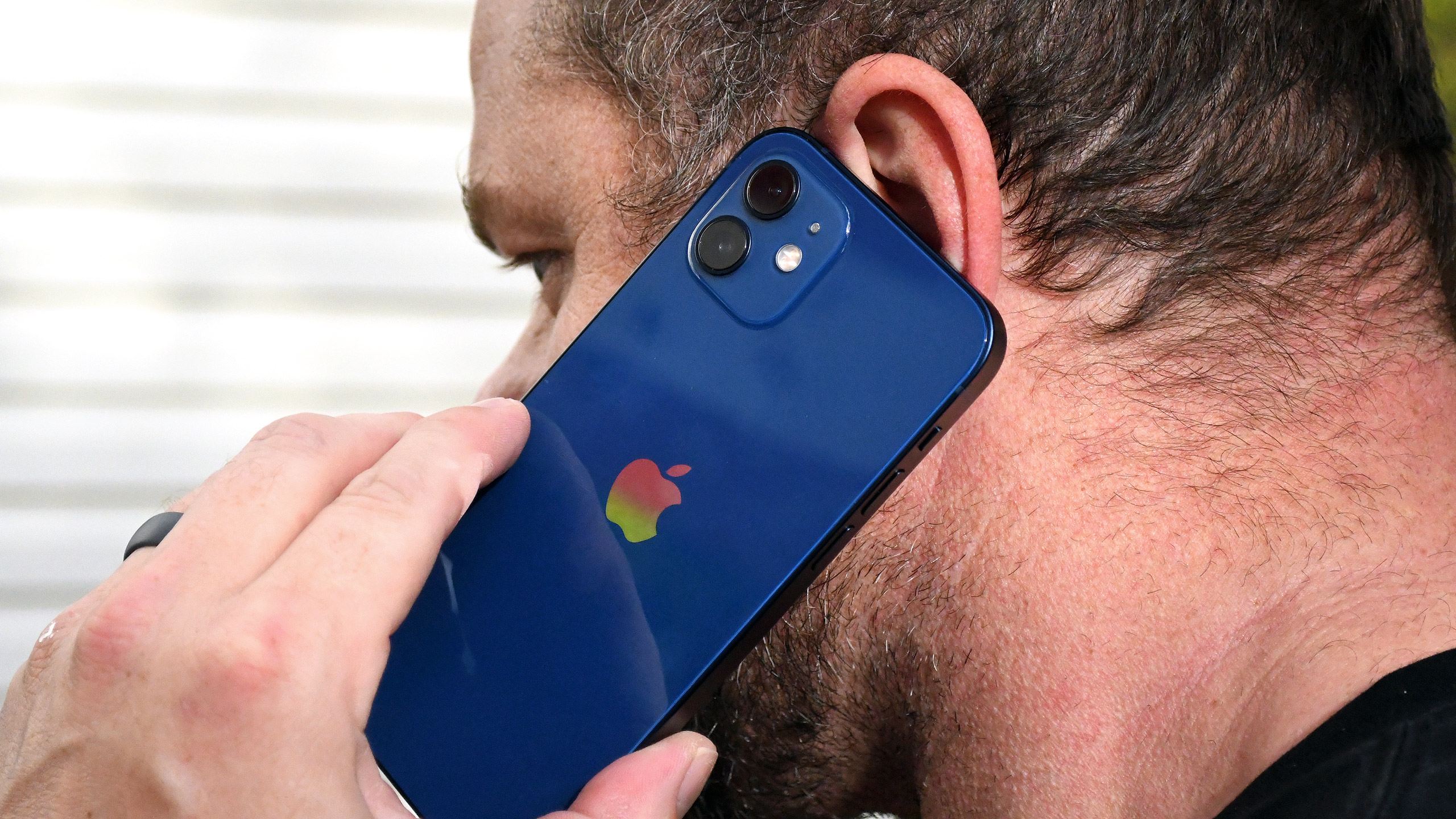 A man making a phone call on a blue iPhone 12