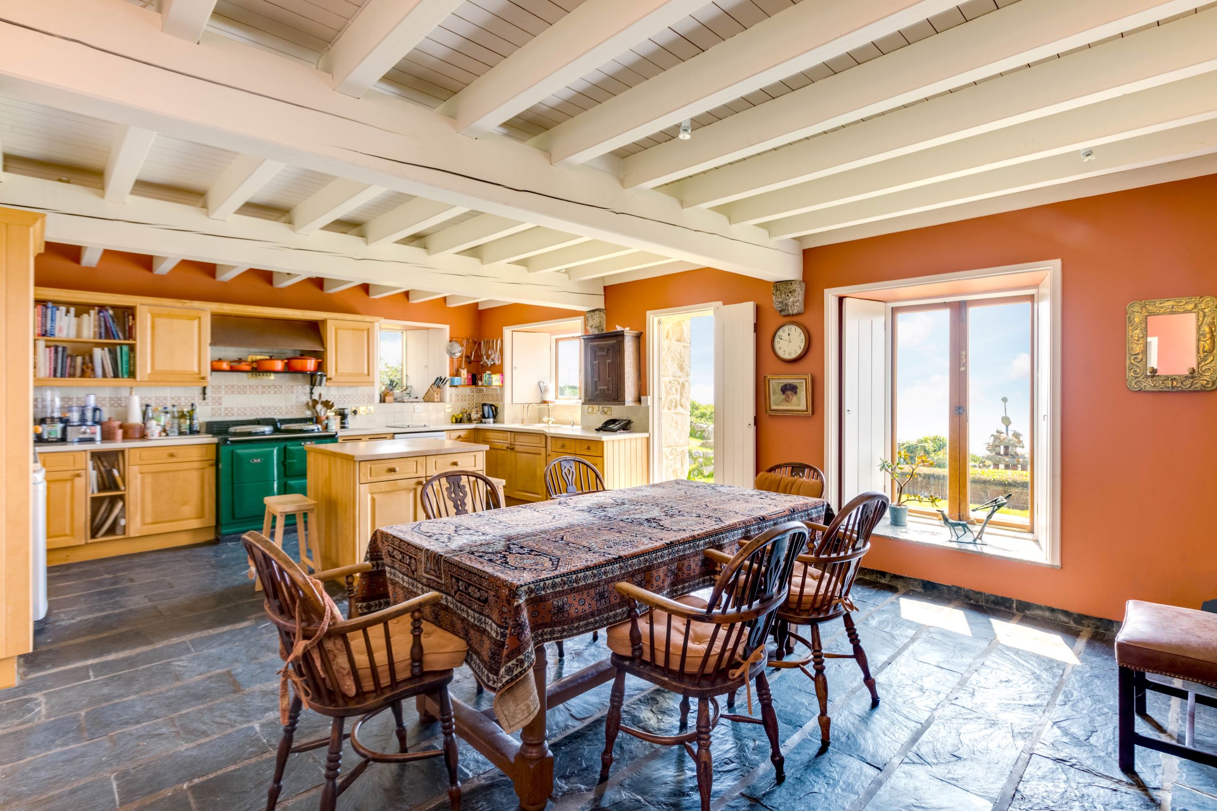 The kitchen has large windows and a dining table with a white marble kitchen island and blue stone flooring