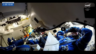 Two astronauts in blue spacesuits wait for launch inside their Boeing Starliner spacecraft