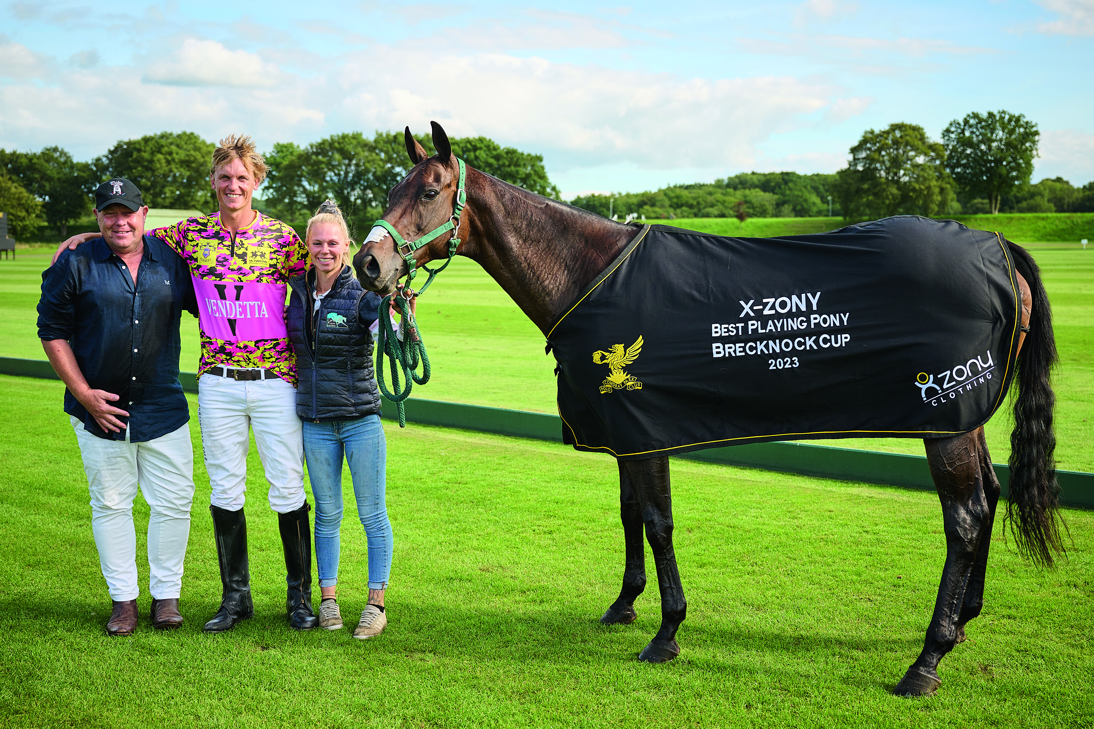 Nick Clague and two others stand next to his pony Bella, who is wearing a fancy jacket that says Best Playing Pony Brecknock Cup 2023