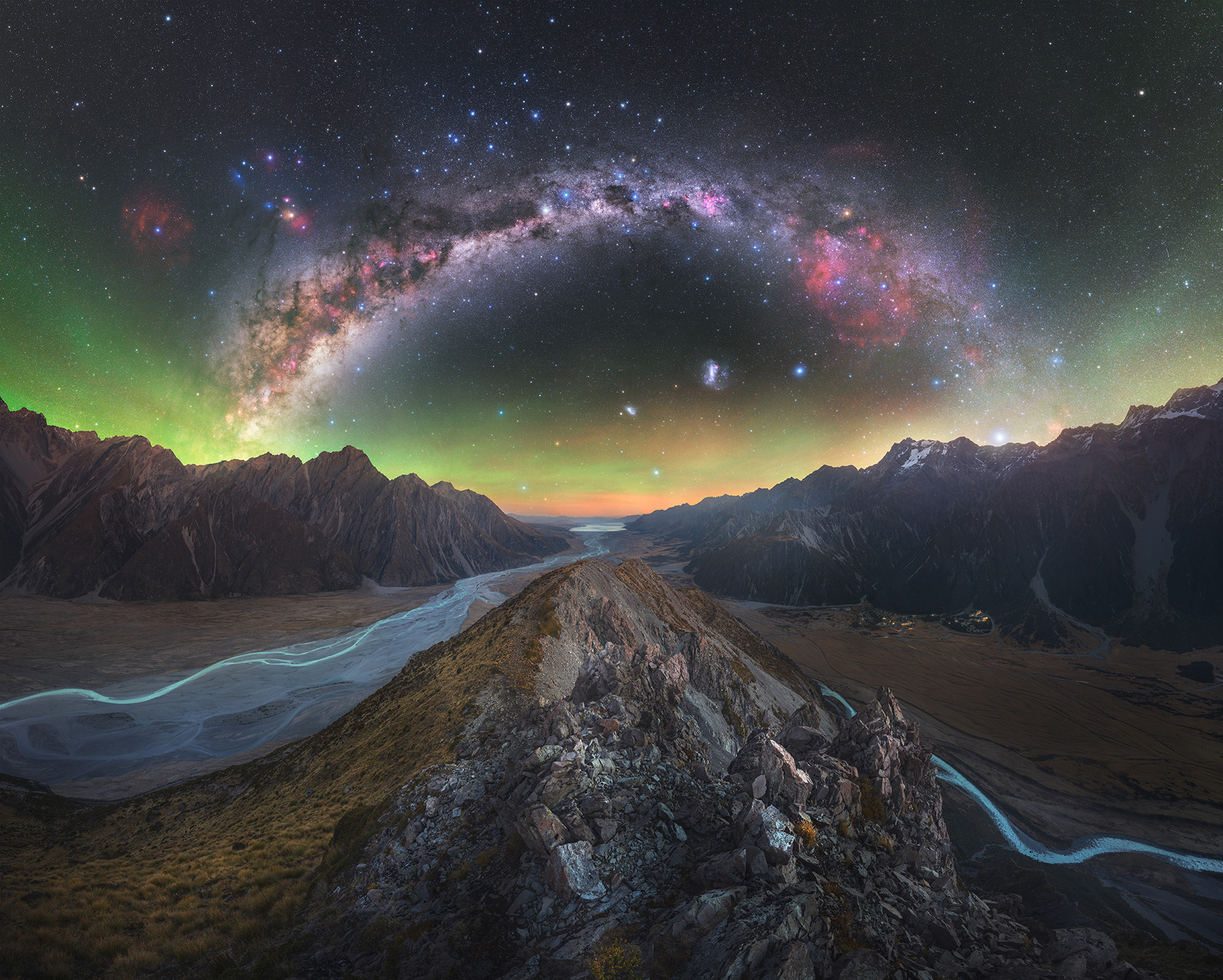 A breathtaking night sky, featuring a vibrant Milky Way arching over jagged mountains and a serene river below, evokes wonder and tranquility