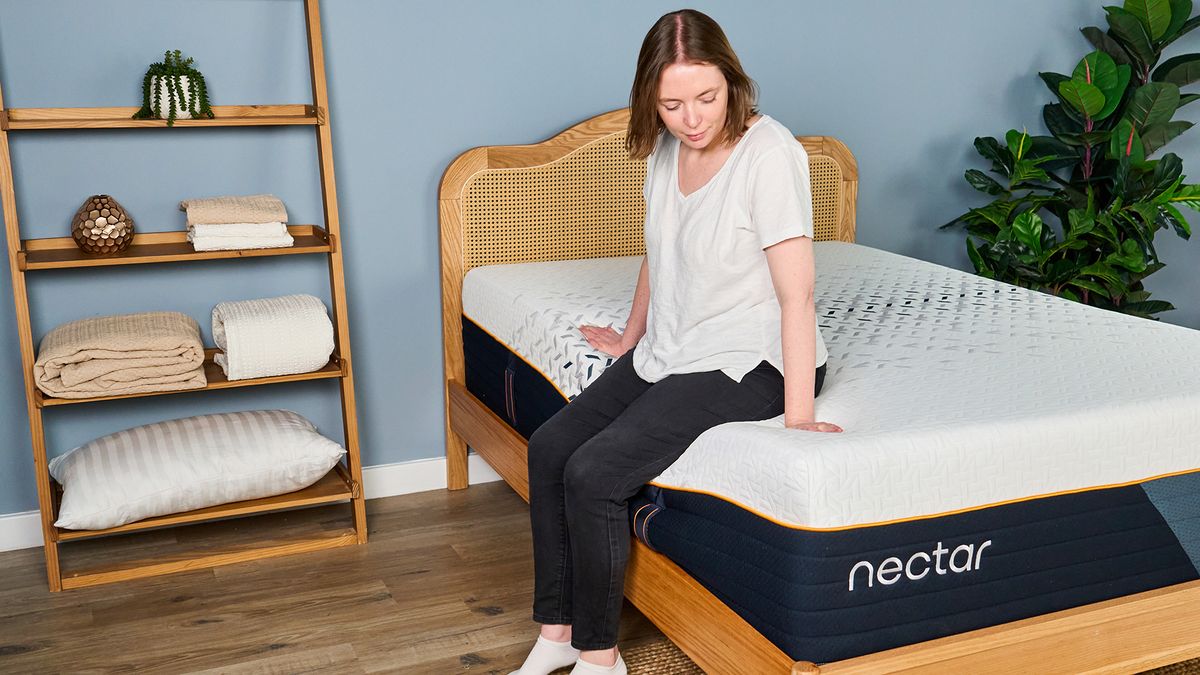 A female Tom's Guide mattress testing sitting on the edge of the Nectar Ultra Hybrid mattress with it visibly sinking beneath her