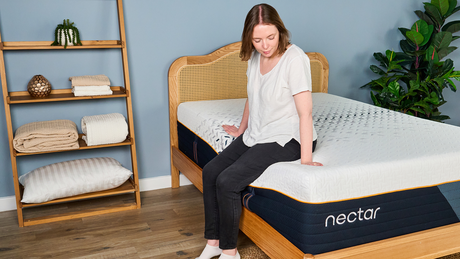 A female Tom's Guide mattress testing sitting on the edge of the Nectar Ultra Hybrid mattress with it visibly sinking beneath her
