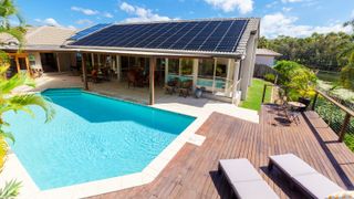 outdoor swimming pool in decked area with roof of nearby building covered in solar panels for pool