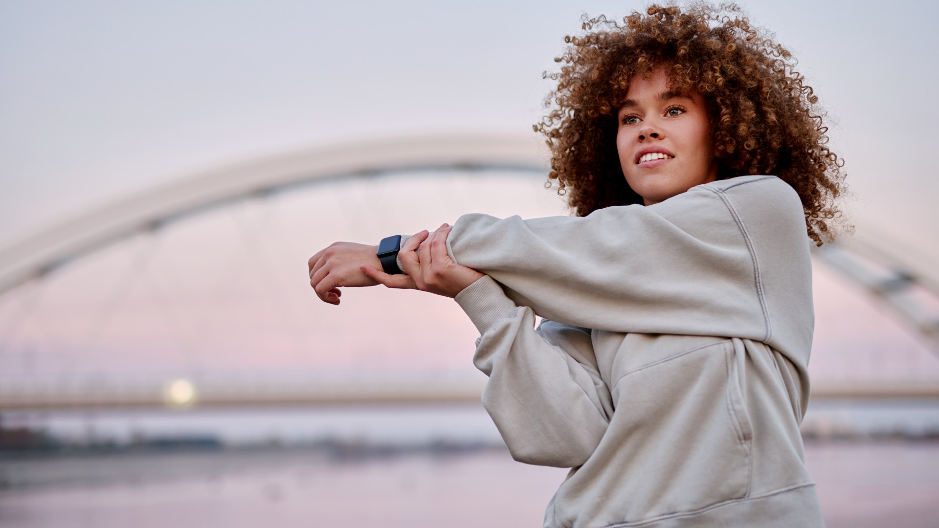 Woman standing outside at sunset stretching her arm across her body